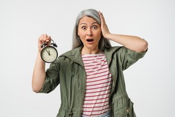 Deadline! Hurry up! Scared mature middle-aged woman grandmother wife holding alarm clock watch feeling shock isolated in white background