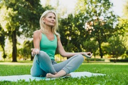Close up portrait of caucasian mature woman in sporty outfit relaxing meditating feeling zen-like on fitness mat in public park outdoors. Healthy active lifestyle