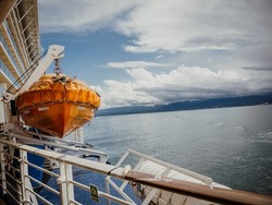 An orange lifeboat hanging over a blue sea on the side of a cruise ship. Rescue boat
