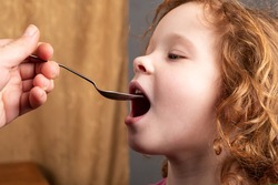 little girl 4 years old drinks cough syrup from a spoon,the child is taking medication closeup.