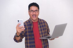 Asian guy in casual clothes, standing with laptop and smartphone in his hands ready to work from home