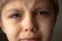Tears in the eyes of a child. The boy is crying and a tear runs down his cheek. Close-up.