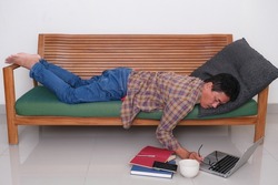 A man lying on a sofa, working on a laptop.