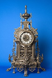 vintage bronze watch on a blue background, bronze fireplace clock, dark old desktop clock on a blue background, antique clock studio photo, antique table bronze clock on a blue background