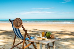 Peaceful beach scenery with a vintage deck chair wooden table, book and coconut s.