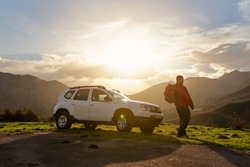 Hiker with backpack watches the sunset on the mountain with his all-terrain car. suv vehicle. Adventure and hiking