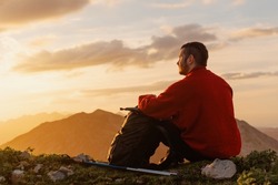 Calm, relaxed hiker man sitting on the mountain contemplating the landscape at sunset after a day of hiking. sports and outdoor activities. healthy life style.