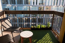 Apartment balcony in city with grass turf and potted plants. Evening light.