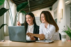 Cheerful female colleagues using laptop together