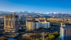 Kyrgyzstan. Bishkek. View from the city to the majestic mountains. Some buildings are still under construction. Construction crane. Mountains with snow. Blue sky. Summer.