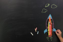 Back to school or Education concept.Top view of kid hand hold blue chalk draw rocket with colorful of color pencil and chalk on chalkboard background.