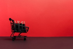 black paper bags in shopping cart on red background, copy space. black friday concept