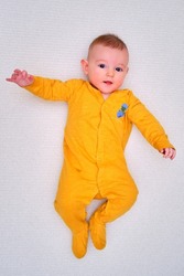 A happy infant baby lying on a play mat in yellow pajamas, top view. Full-length smiling toddler on white floor, copy space