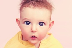 Curious toddler baby boy with big eyes on a pink background, face close-up. Portrait of a confused child with disheveled hair