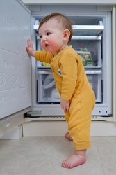 Toddler baby boy with allergies on red cheeks climbed into an open refrigerator. Child safety issues in the home room, little kid