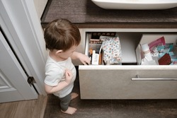 Toddler baby pulls out an item drawer in a home bathroom. A small child explores the closet in the bathroom. Kid aged one year eight months