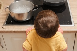 Child reaches for the hot stove with a pot of boiling water. Baby safety issues in the home room. Kid aged two years