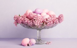 Transparent bowl  with  Easter eggs and flowers of Lilac  on pale light violet  background.  Easter decor