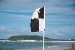 Black and white surf craft flag flying on patrolled beach at Coffs Harbour on summer day