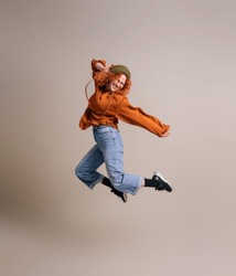 Funky young woman jumping ecstatically in air and celebrating achievement against background