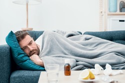 Man wrapped in plaid lying on the sofa feeling sick illness at home