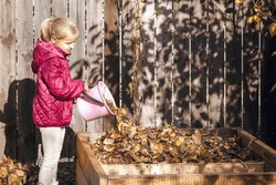 Compost Autumn from Fallen Leaves. Child Little Girl Throwing Dried Fall Leaves into Compost Bin Container. Autumn Cleaning Garden.