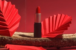 Red lipstick on wooden podium with paper craft and glass on red background. Creative concept photo of cosmetics with hard shadow