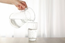 Pouring purified fresh water from the jug in glass on wooden table