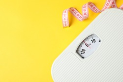 Scales and measuring tape on yellow background. Weight loss concept