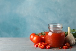 Jar with red chilli and tomato sauce, and spices on wooden table