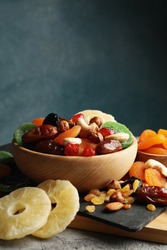 Board and bowls with dried fruits and nuts on gray background