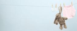 Child clothes and toy hanging on twine against light background