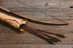 Close up shot of bow laying beside arrows in a leather quiver on wooden planks