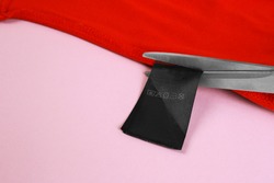 A pair of scissors cutting a tag off. Tag trim on baby clothes, close up.Tags that pierce the skin