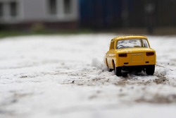 close up a yellow metal small car stands on the snow outside side view . toy on the street