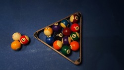 Pool game sport on green cloth.  Multi-colored billiard balls in triangle shape with numbers, two cues, cue balls and triangles on the pool table.  Billiards billiard ball close up.