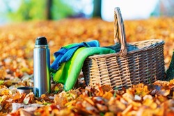 A wicker basket metal steel thermos and a cup with a hot drink, tea, coffee stands on a autumn leaves background in nature picnic autumn forest.Selective focus,blured background.