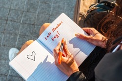 Woman writes in a notebook, holds felt-tip pen in her left hand.Outdoors summer evening park. Left-handers Day August 13th.Closeup.