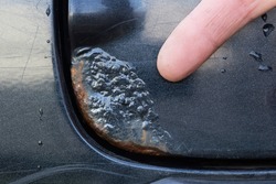 Corrosion of metal on the car body. The finger points to a rusting part of the car.