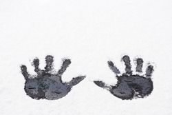 Black prints of human hands on white snow. Shallow depth of field.