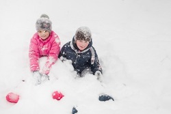 Mädchen und Junge spielen im Tiefschnee. Es liegt starker Schnee. Es gibt kleine weiße Schneeflocken ganz über dem Rahmen.