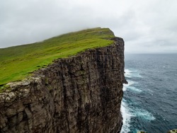 Steep cliffs of Faroe Islands. Green grass at the top, Ocean below the cliffs. 