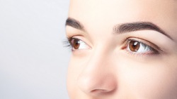 Woman with beautiful eyebrows close-up on a light background with copy space. Microblading, microshading, eyebrow tattoo, henna, powder brows concept.