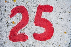 Number 25 painted with red paint on gray concrete.Abstract writing number 25 on concrete. Quarter symbol.25 percent discount. Concrete numbers.Number 25 on the wall