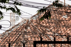 the roof of an old urban house. silhouettes of stretched electric wires, leaves and iron fences. tower and white sky in the background