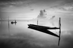 Black & white scenery of traditional fishing boat at Tumpat, Malaysia with fisherman silhouette standing on the boat. Soft focus due to long exposure.  