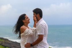 A young lovely attractive couple looking at each other, embracing, making love, smiling, cuddling at beach on vacation, holiday, honeymoon, trip to India, Maldives, Asia, foreign beach, cliff, sunset.