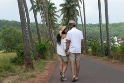 Beautiful young lovely attractive tourist couple looking each other, embracing, making love, smiling, cuddling walking on Parra Coconut road in Goa with palm trees fields. Love you Dear Zindagi road.