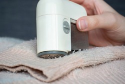 Pilled sweater. Woman hand using handheld electric fabric shaver fuzz remover device machine for removing fuzz, lint and pills (pilling) on clothes