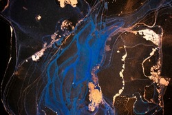 Luxury abstract fluid art painting in alcohol ink technique, mixture of white, blue and gold paints on black paper. Imitation of marble stone cut, glowing golden veins. Tender and dreamy design.